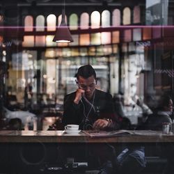 Man using phone on table in cafe seen through window