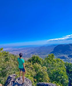 Rear view of man standing on mountain against blue sky