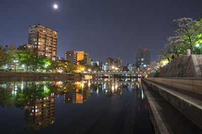 Illuminated city by buildings against sky at night