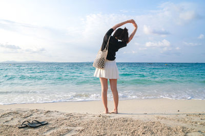 Rear view of person standing at beach against sky