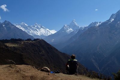 Rear view of man sitting against snowcapped mountains