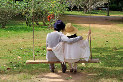 Rear view of couple in hats sitting on swing in park