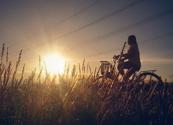 Man sitting on field against sky during sunset
