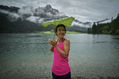 Smiling woman holding green leaf while standing at haldensee lakeshore during rainy season