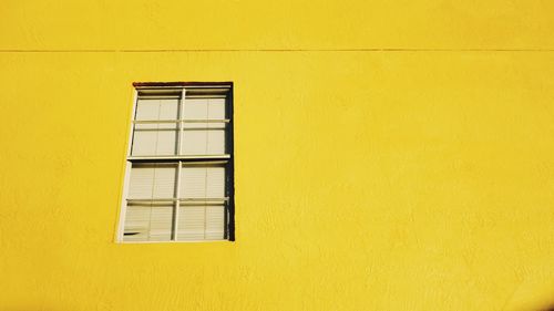 Low angle view of window on yellow wall