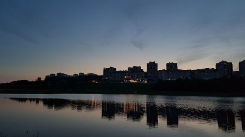 Silhouette buildings by lake against sky during sunset