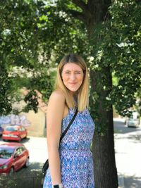 Portrait of smiling young woman standing against trees