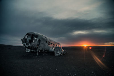 Abandoned airplane on land against sky during sunset