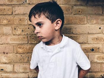 Close-up of boy looking away while standing against brick wall