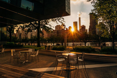 Empty chairs and tables against buildings during sunset