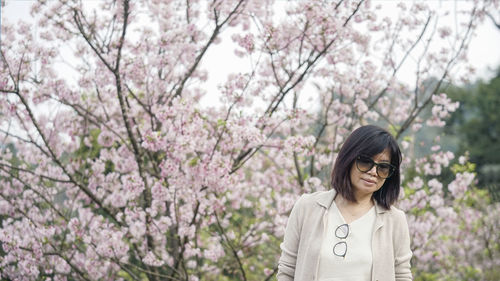 Portrait of young woman standing by cherry blossom tree