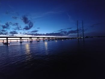 Silhouette bridge over sea against blue sky