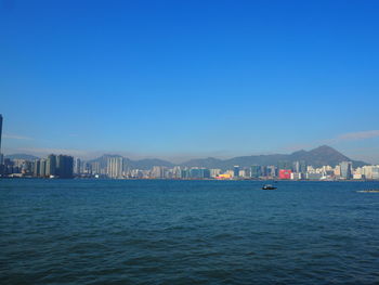 Sea by cityscape against clear blue sky