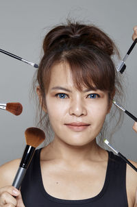 Portrait of woman amidst cropped hands with brushes over gray background