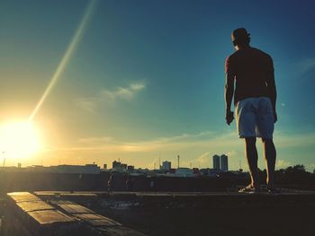 Rear view of man walking on street against sky during sunset