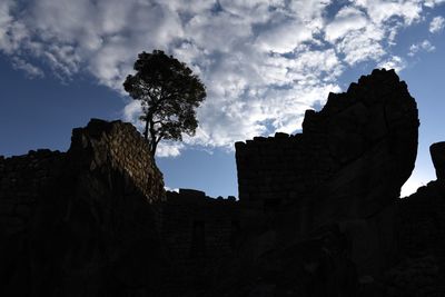 Low angle view of silhouette rock formation and buildings against sky