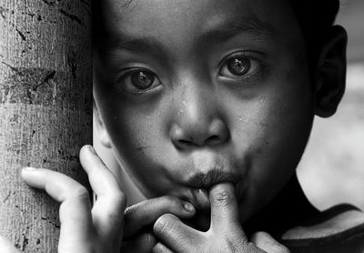 Close-up portrait of boy with finger in mouth by tree trunk