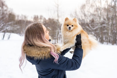 Young woman carrying dog while standing in snow during winter