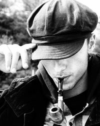 Close-up of young man smoking pipe while wearing cap