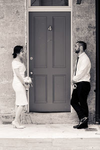 Side view of smiling couple standing against closed door of building