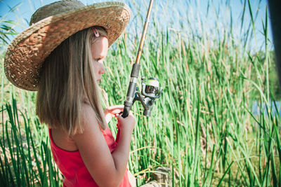 Side view of girl holding fishing rod against grass