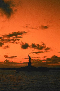 Silhouette person by sea against sky during sunset