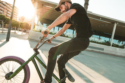 Full length of young man riding bicycle on road against sky during sunset