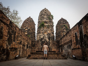 Rear view of man standing in front of buddhist temple, sukhothai, thailand