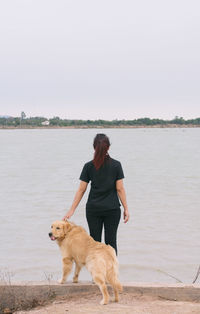 Rear view of man with dog on beach against sky