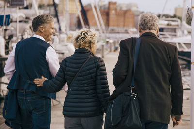 Rear view of senior friends in warm clothing walking on pier