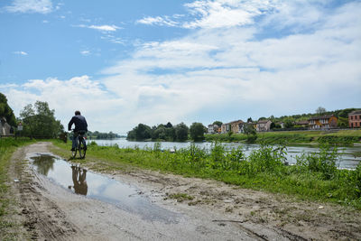Rear view of man riding bicycle on canal against sky