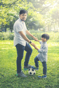 Portrait of father with son standing with soccer ball at park