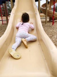 Rear view of girl sitting on slide at playground