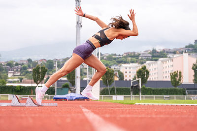 Full body side view of determined young female sprinter starting to run from blocks on track of stadium