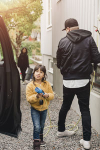 Girl helping father in charging electric car while going for picnic