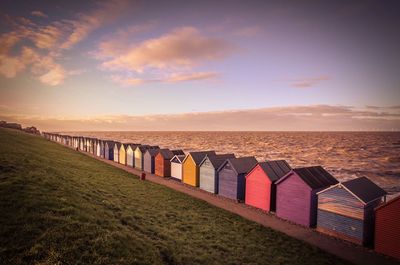 Colorful beach huts on beach against cloudy sky