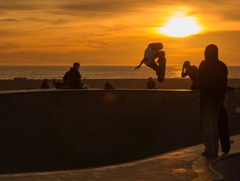 Silhouette people on beach against sky during sunset