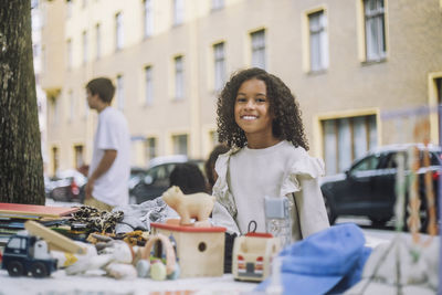 Portrait of smiling elementary girl standing near stall at flea market