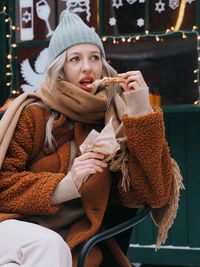 Young  woman with blonde hair wearing brown fur coat eating sweet food on the christmas market.