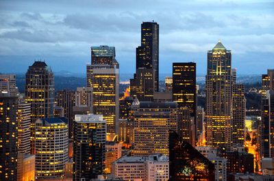 View of skyscrapers lit up against cloudy sky