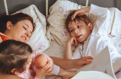 High angle view of mother telling bed time story to children on bed at home