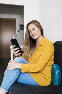 Young woman using mobile phone while sitting on sofa at home