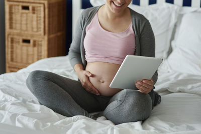 Midsection of woman sitting on bed at home