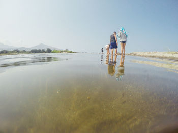 Rear view of people walking on shore against clear sky