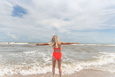 Rear view of young woman with arms outstretched standing on shore at beach