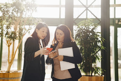 Confident female colleagues discussing over smart phones at office