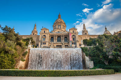 Fountain in front of building against blue sky