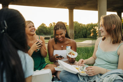 Happy teenage girls talking with each other while enjoying food at park