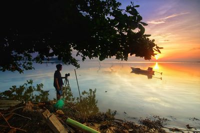 Reflection of man in lake against sky during sunset