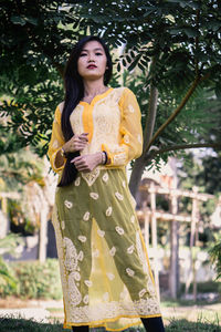 Beautiful young woman standing against yellow and plants